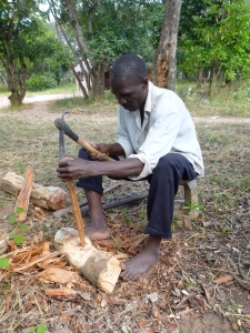 Ba Allan Mwango carving wooden cooking sticks. He owns a few pairs of shoes, but rarely wears them around the house.