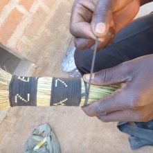 Mwila making a broom from dried grasses and sliced up bits of bike tubing.