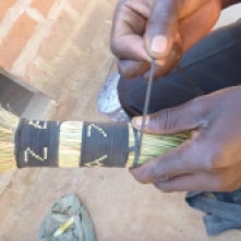 Mwila making a broom from dried grasses and sliced up bits of bike tubing.