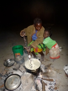 Ba Agatha talking with her daughter Gile while cooking ubwali over a traditional three-stone fire.