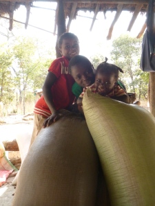 Joyci, Stephen, and Gile goofing around atop some maize sacks in their family's nsaka.