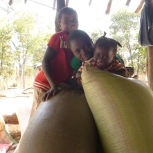 Joyci, Stephen, and Gile goofing around atop some maize sacks in their family's nsaka.