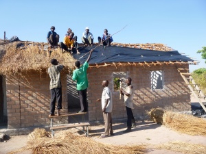 Putting plastic and grass thatch over the Mfuba Community School roof.